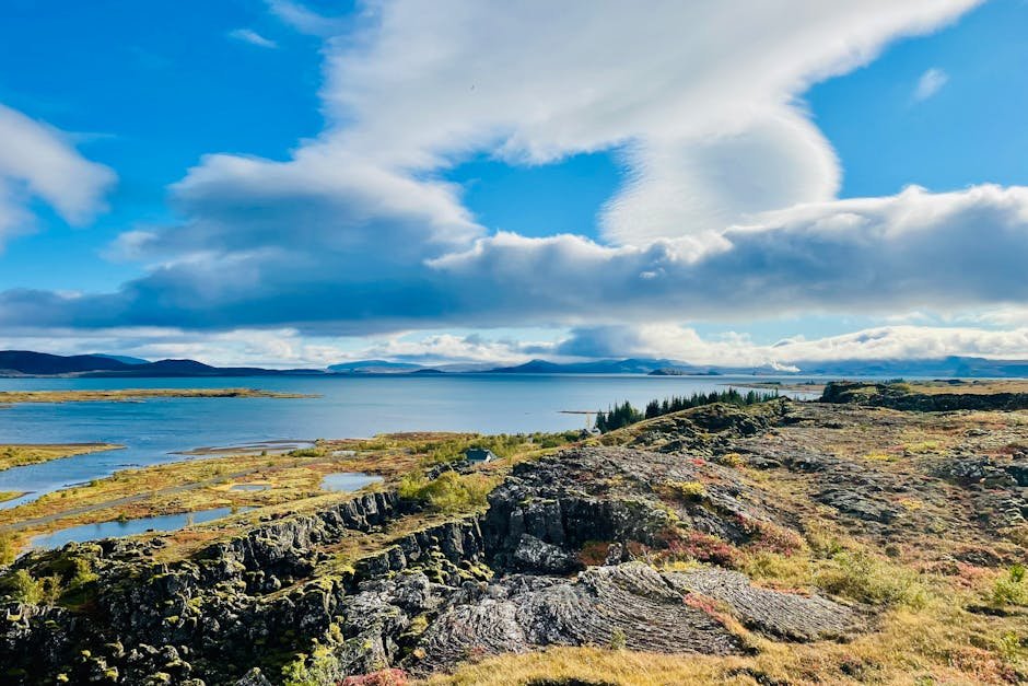 Vista paesaggistica mozzafiato del Parco Nazionale di Þingvellir con scogliere e lago sotto un cielo azzurro.