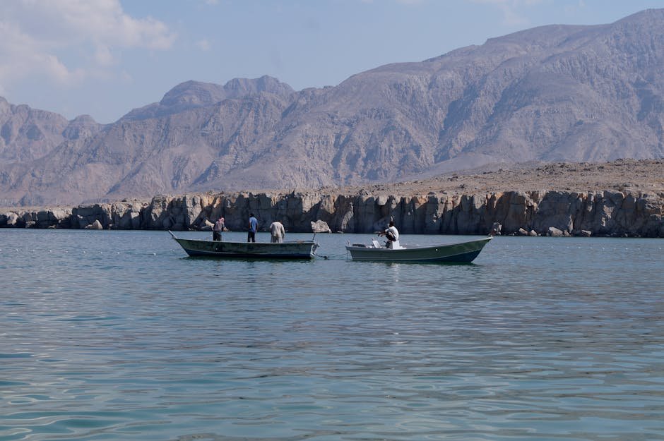 Fishermen on boats against the dramatic backdrop of Musandam's mountains and serene waters.