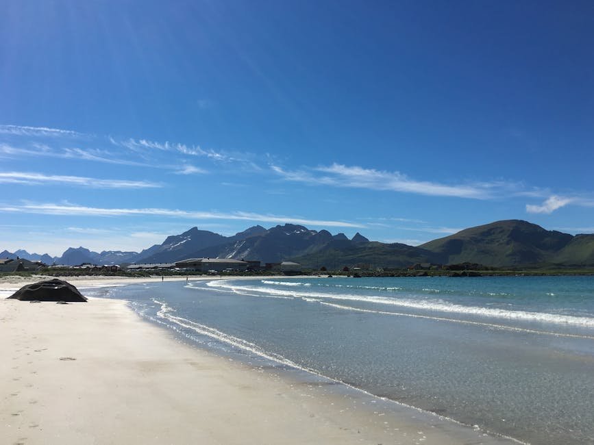 Scena soleggiata sulla spiaggia di Ramberg, Norvegia, con montagne e cielo azzurro limpido.