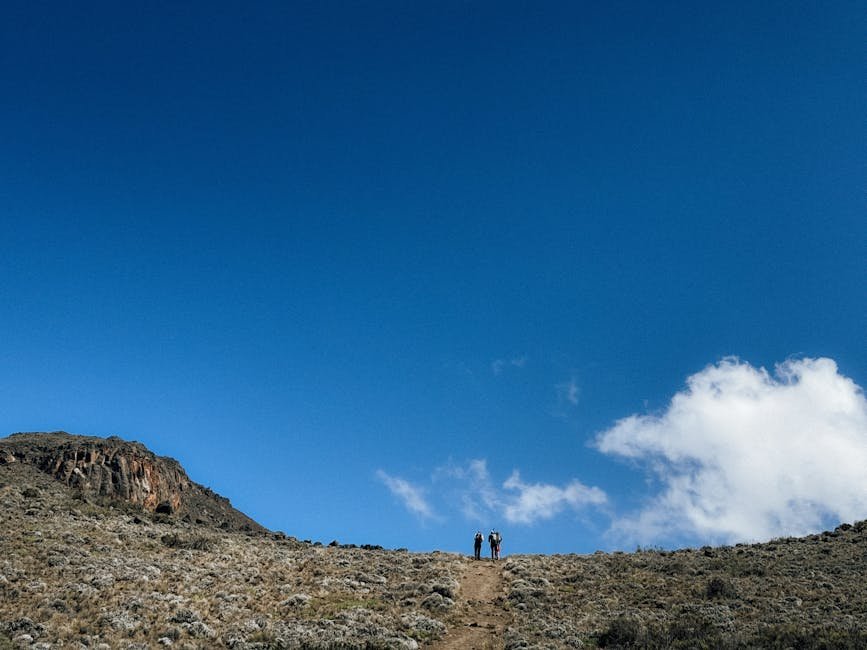 Due escursionisti salgono un sentiero roccioso sotto un vasto cielo azzurro vicino al Monte Kilimanjaro, Tanzania.